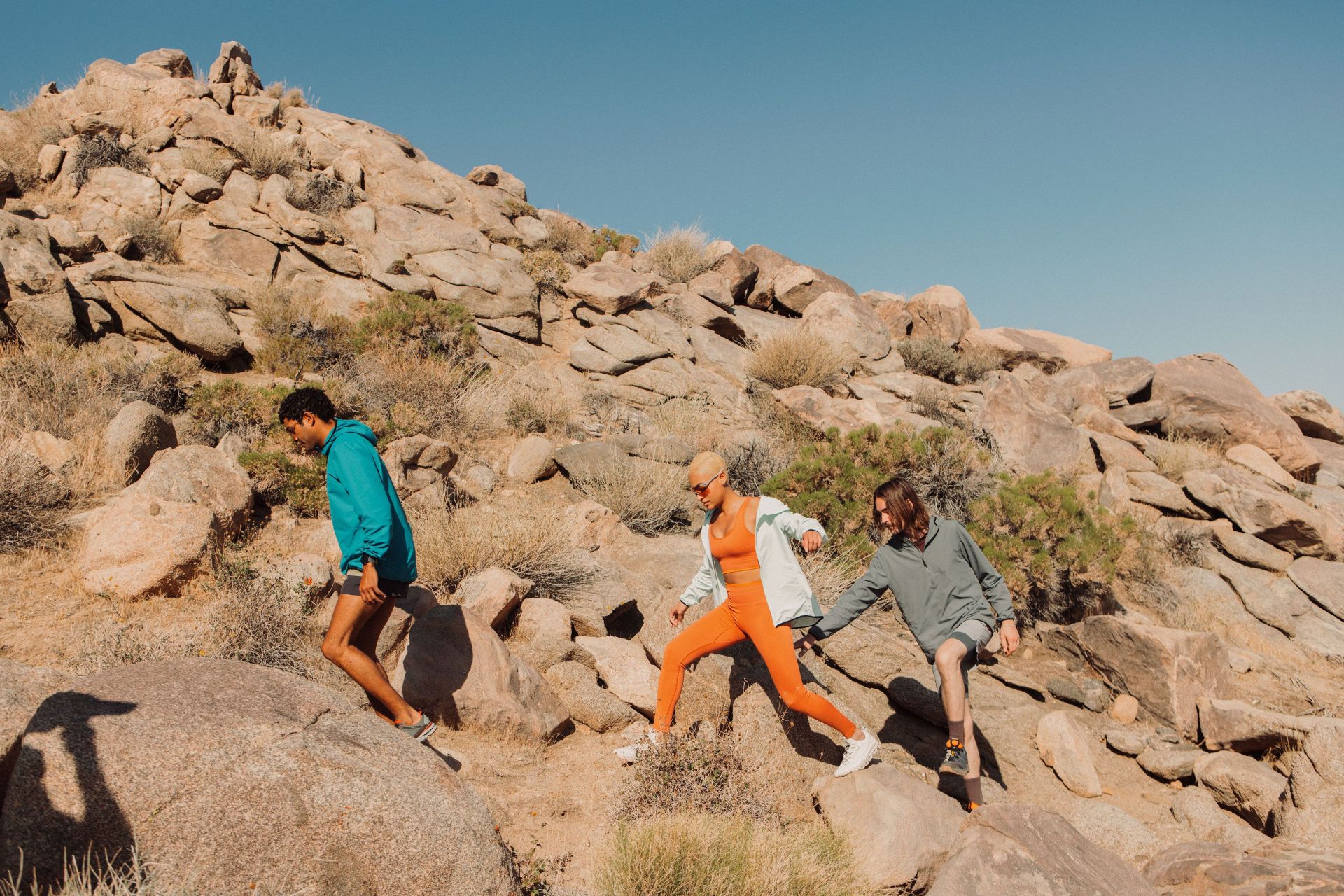 a man and two women hiking up rocky terrain wearing coollife clothing