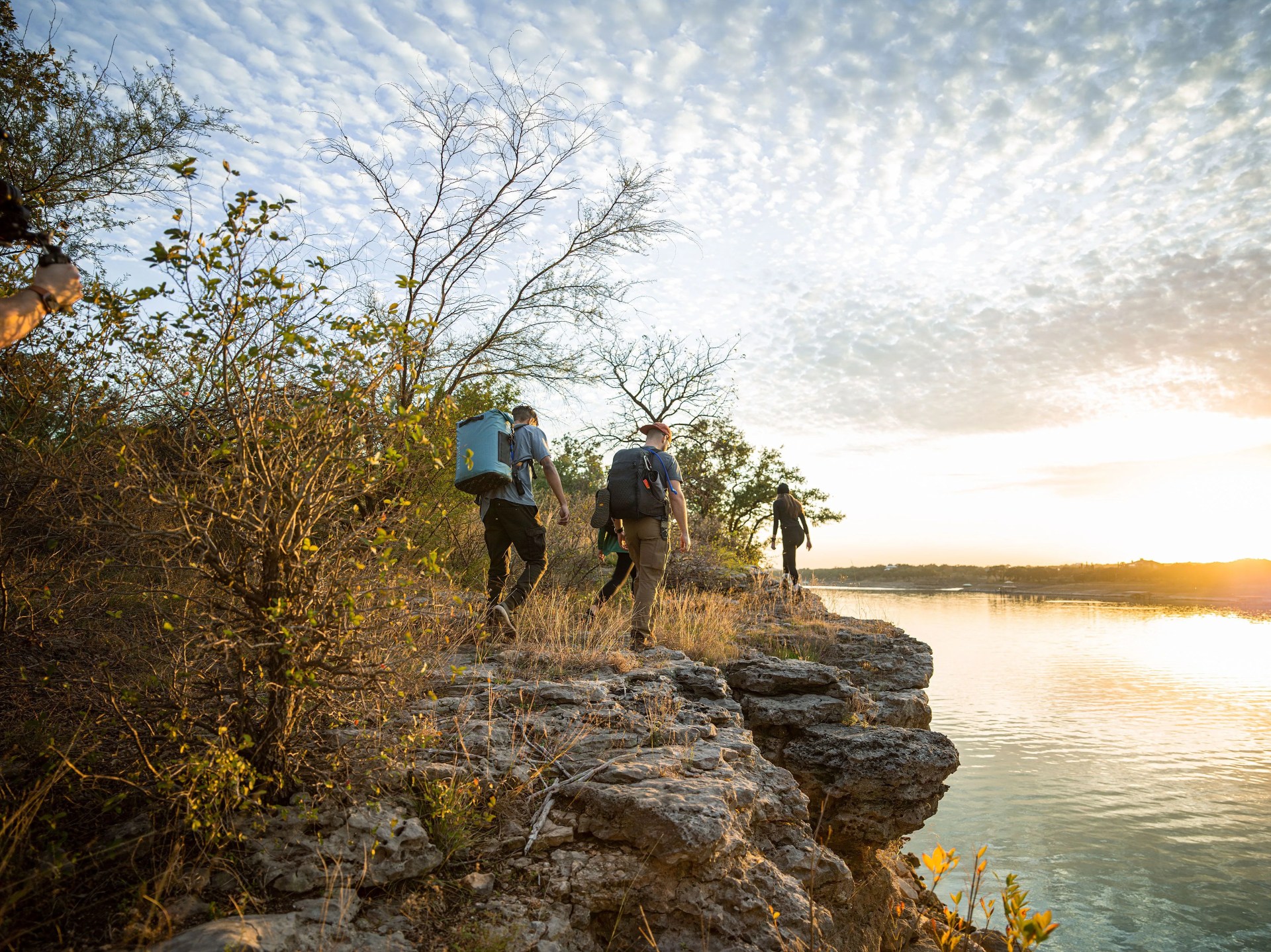 two men and a woman hiking along rocky terrain by water carrying camelbak chillbak pack 30