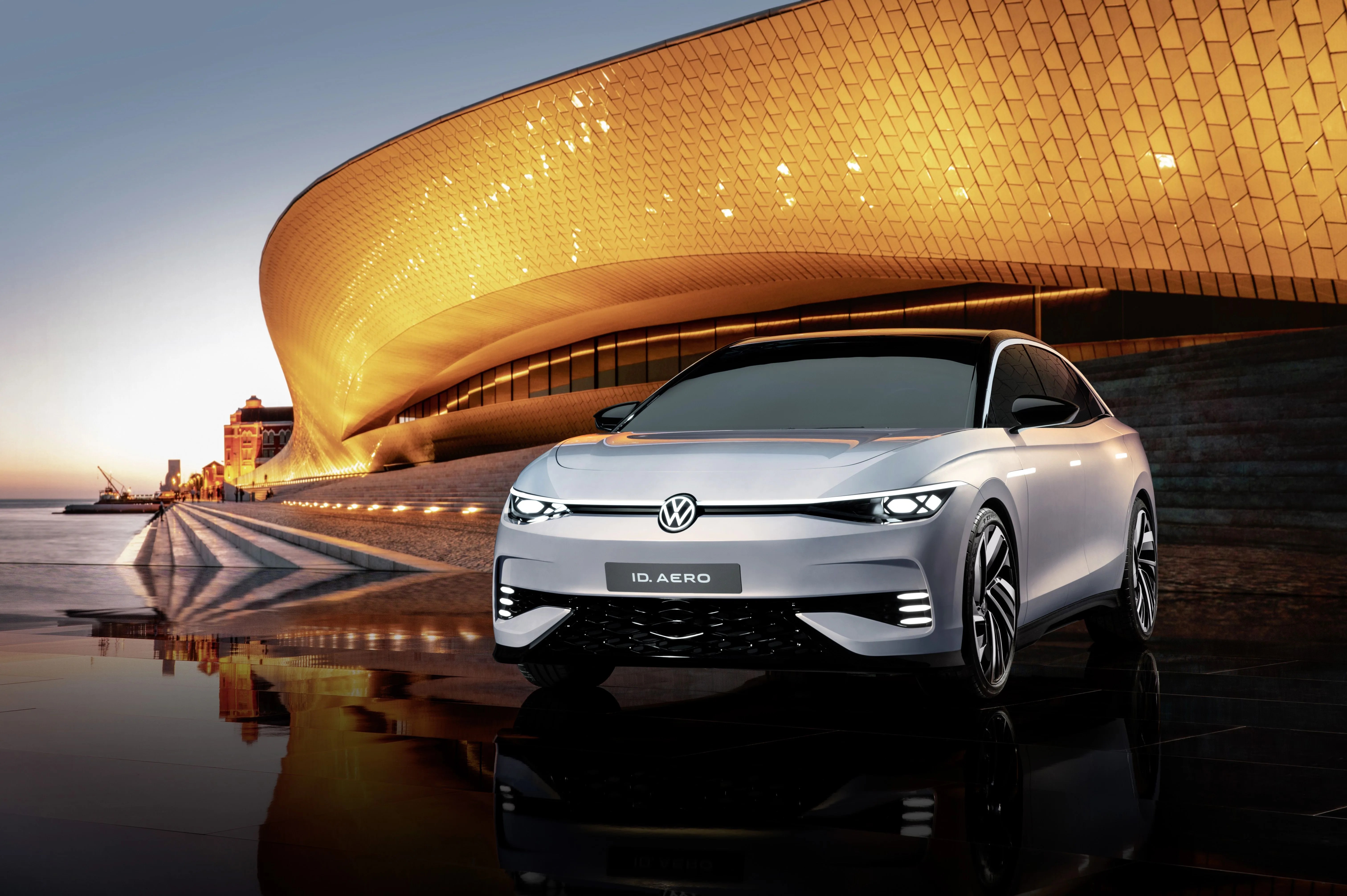 volkswagen id aero parked in front of a futuristic building along the waterfront