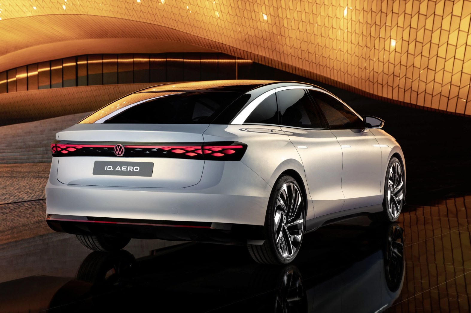 vw id aero sedan shot from the rear with a futuristic building in the background