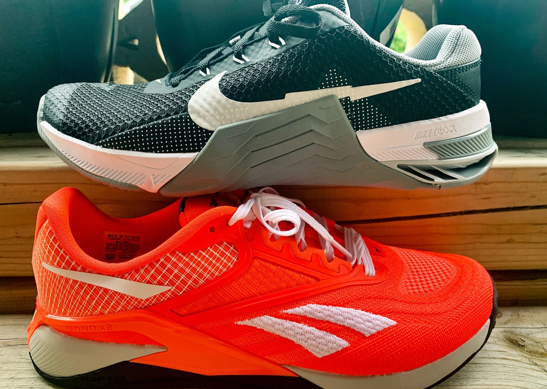 black and white nike metcon 7 shoe sitting on top of a red and white reebok nano x2 shoe