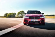 frontal shot of bmw m5 rounding the corner on a track with trees and a field in the background