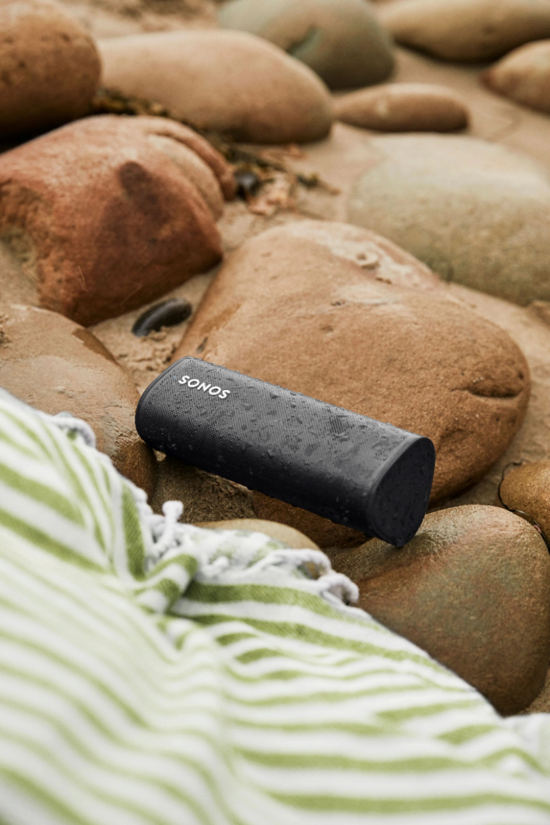 sonos roam wet sitting on rocks next to beach towel