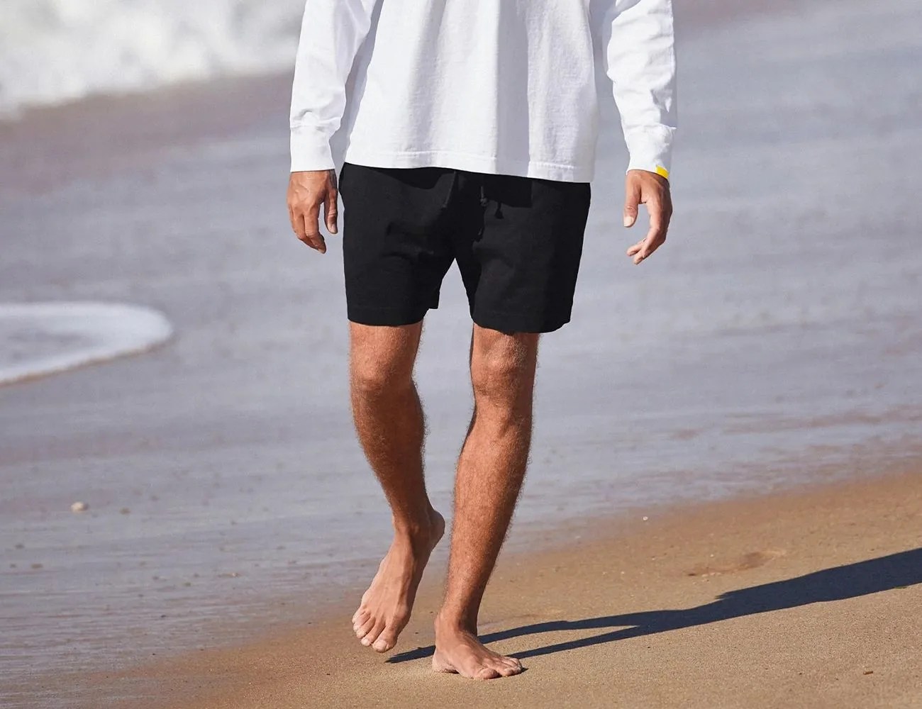 man walking on beach in black shorts and white long sleeve shirt