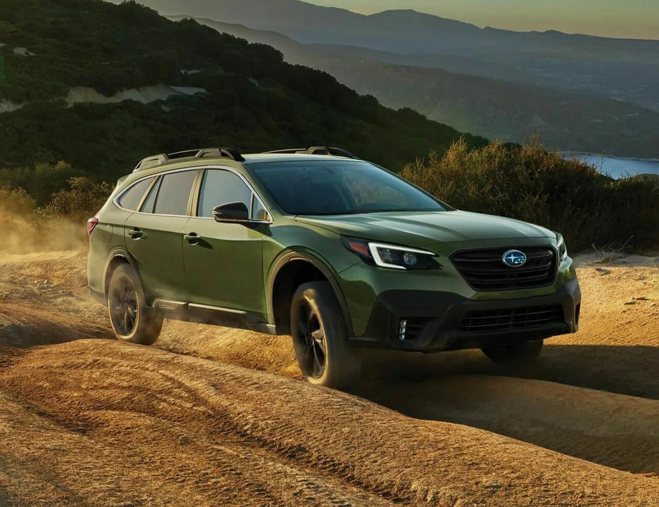 subaru outback driving on an off road mountain trail with mountains and water in the background