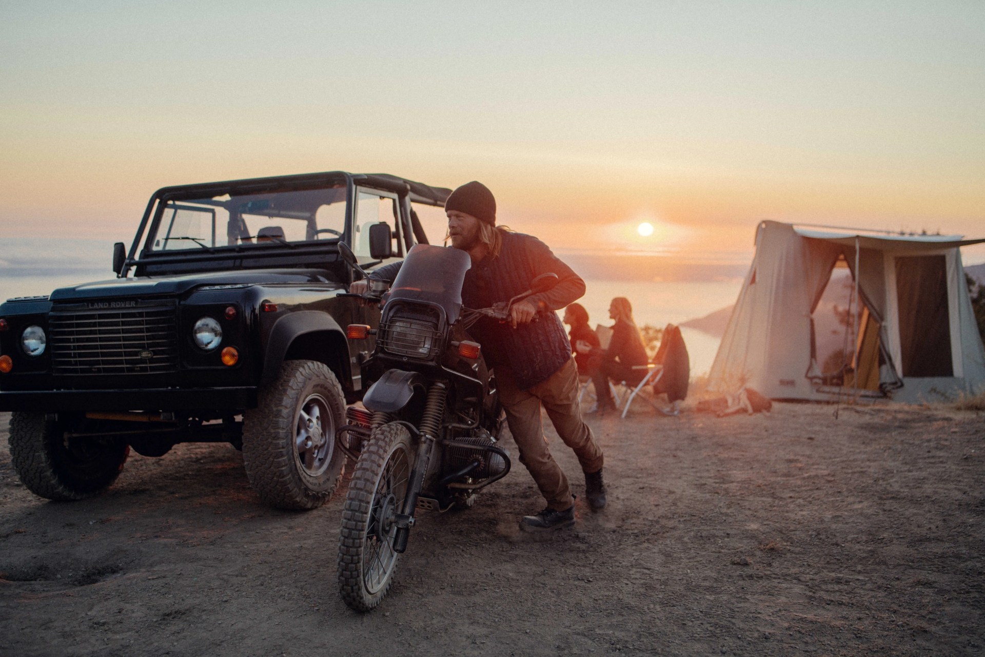 man pushing motorbike across beach wearing aether gear