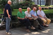 elderly men sitting on a park bench talking to a man standing by his bike