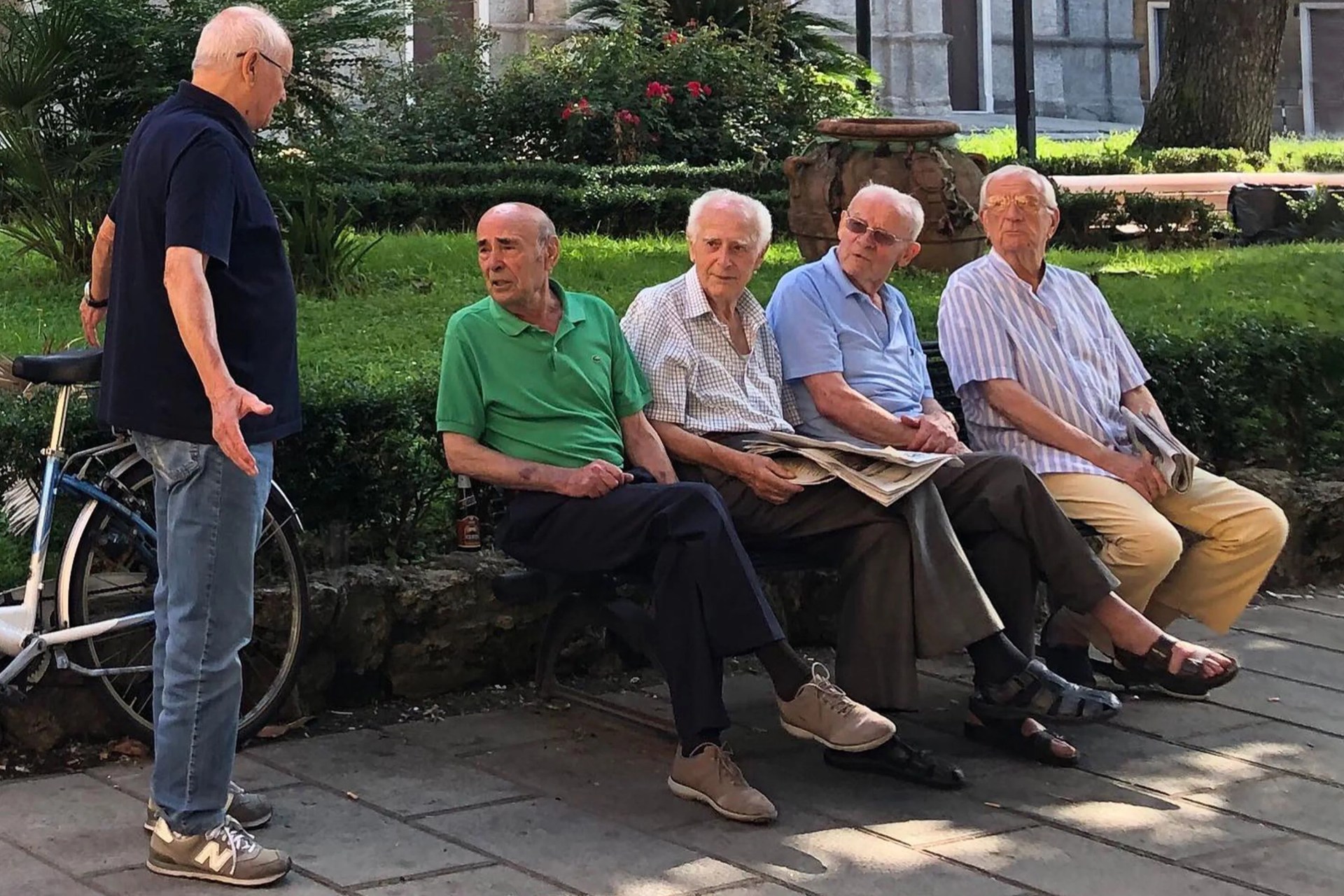 elderly men sitting on a park bench talking to a man standing by his bike