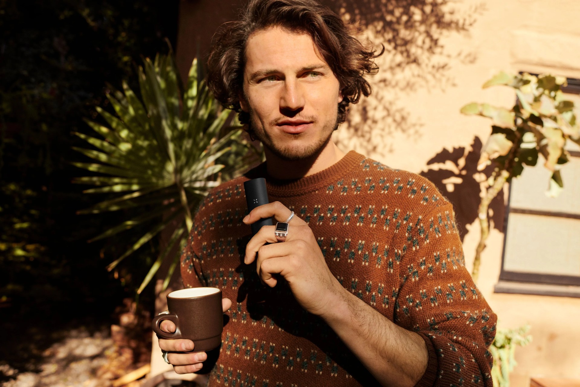 man holding pax vape in one hand with mug in other hand