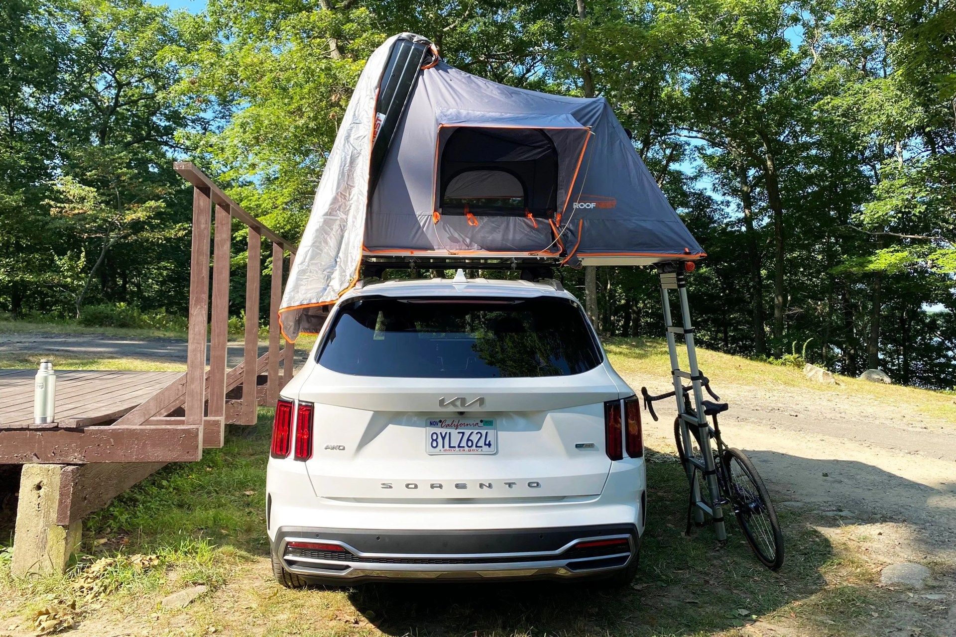 backside of the roofnest condor xl tent opened on top of a white kia sorento with a gravel bike leaning against the tent ladder