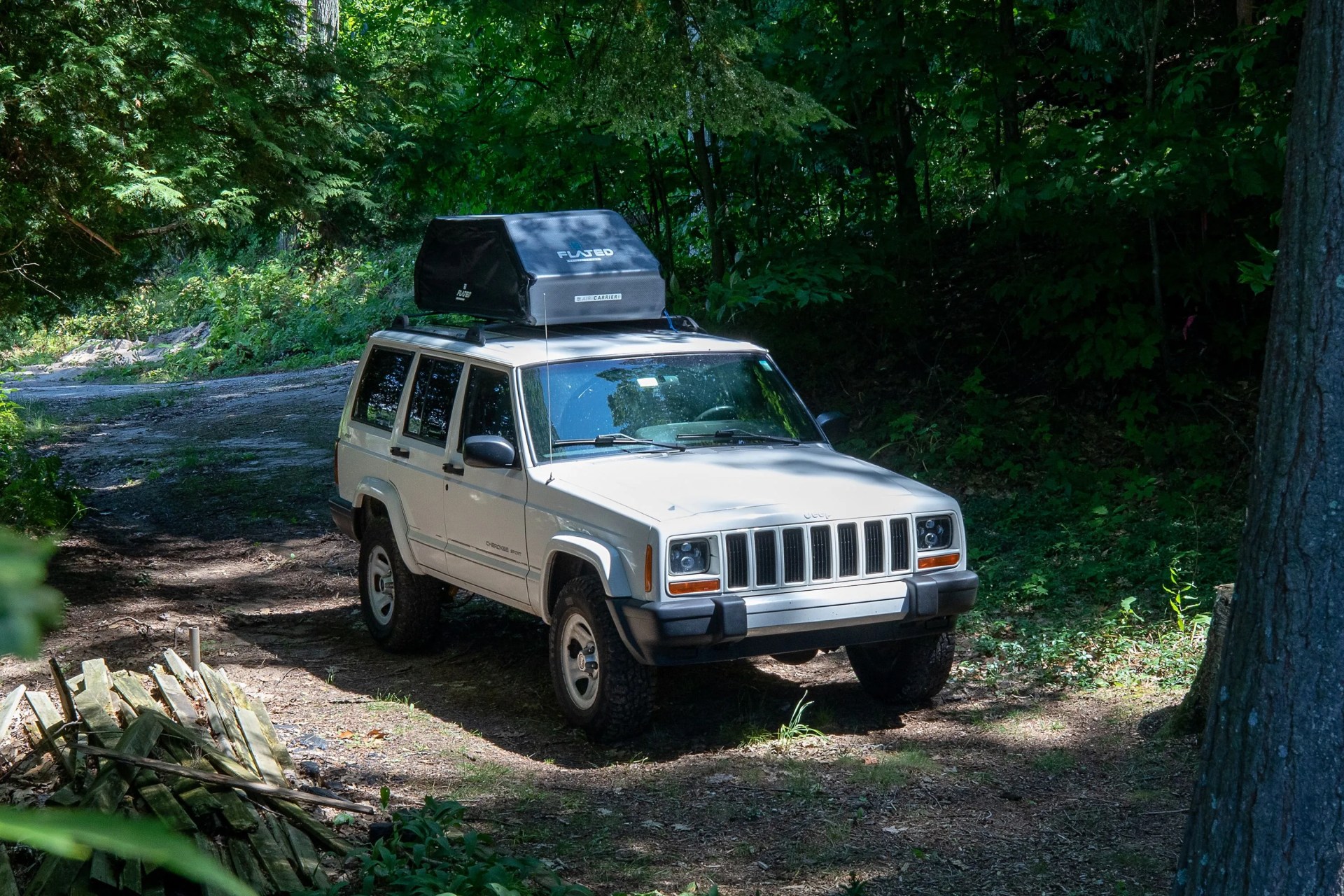 white jeep parked in a dirt driveway with a flated air carrier on top