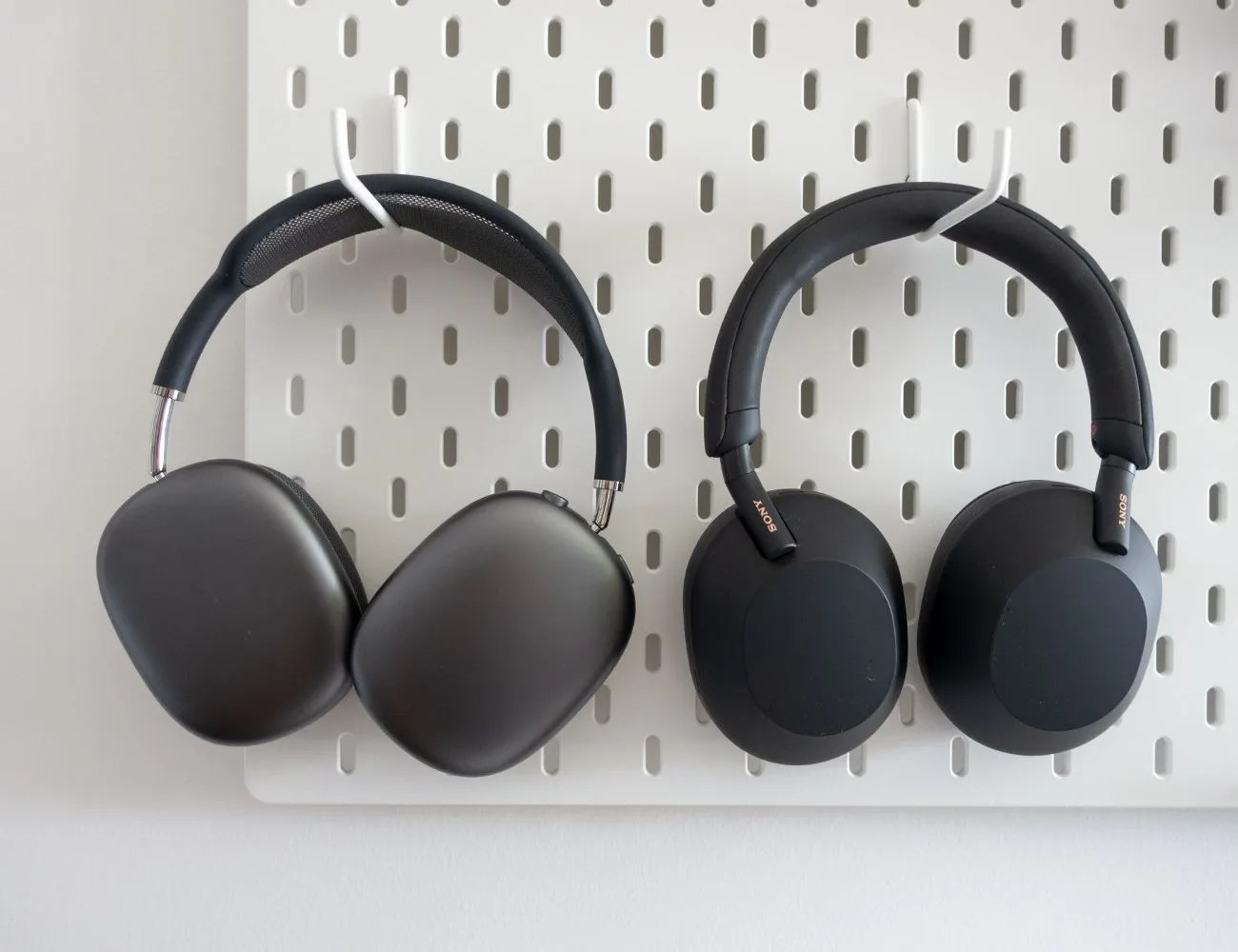 black sonywh 1000xm5 and black apple airpod max headphones hanging from white peg board