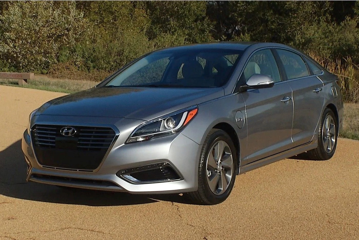 hyundai sonata hybrid parked on pavement in front of woods