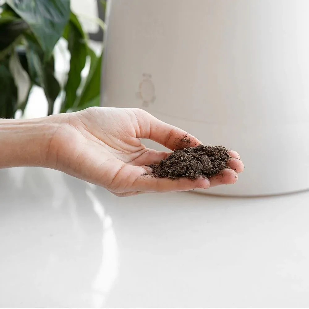a hand holding dirt from a countertop composter