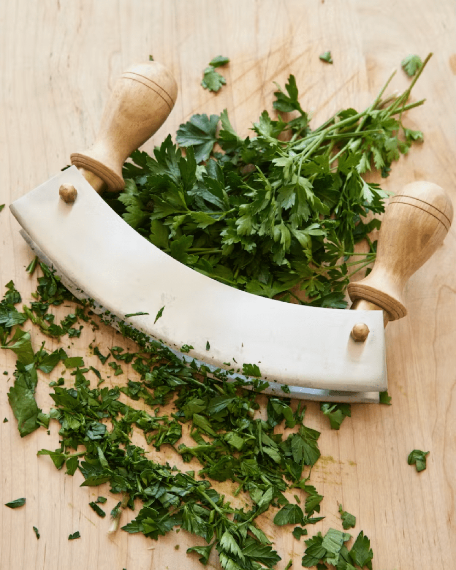 sir madam’s new double mezzaluna chopper on a wood cutting board with fresh herbs
