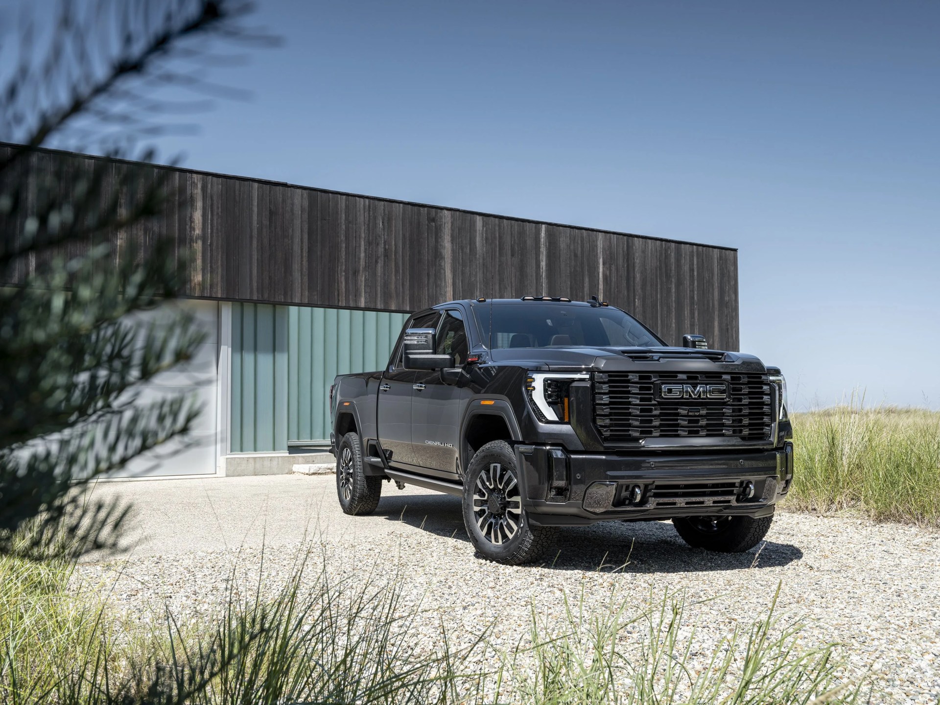 gmc sierra denali hd ultimate pickup parked on gravel next to a modernist wood house