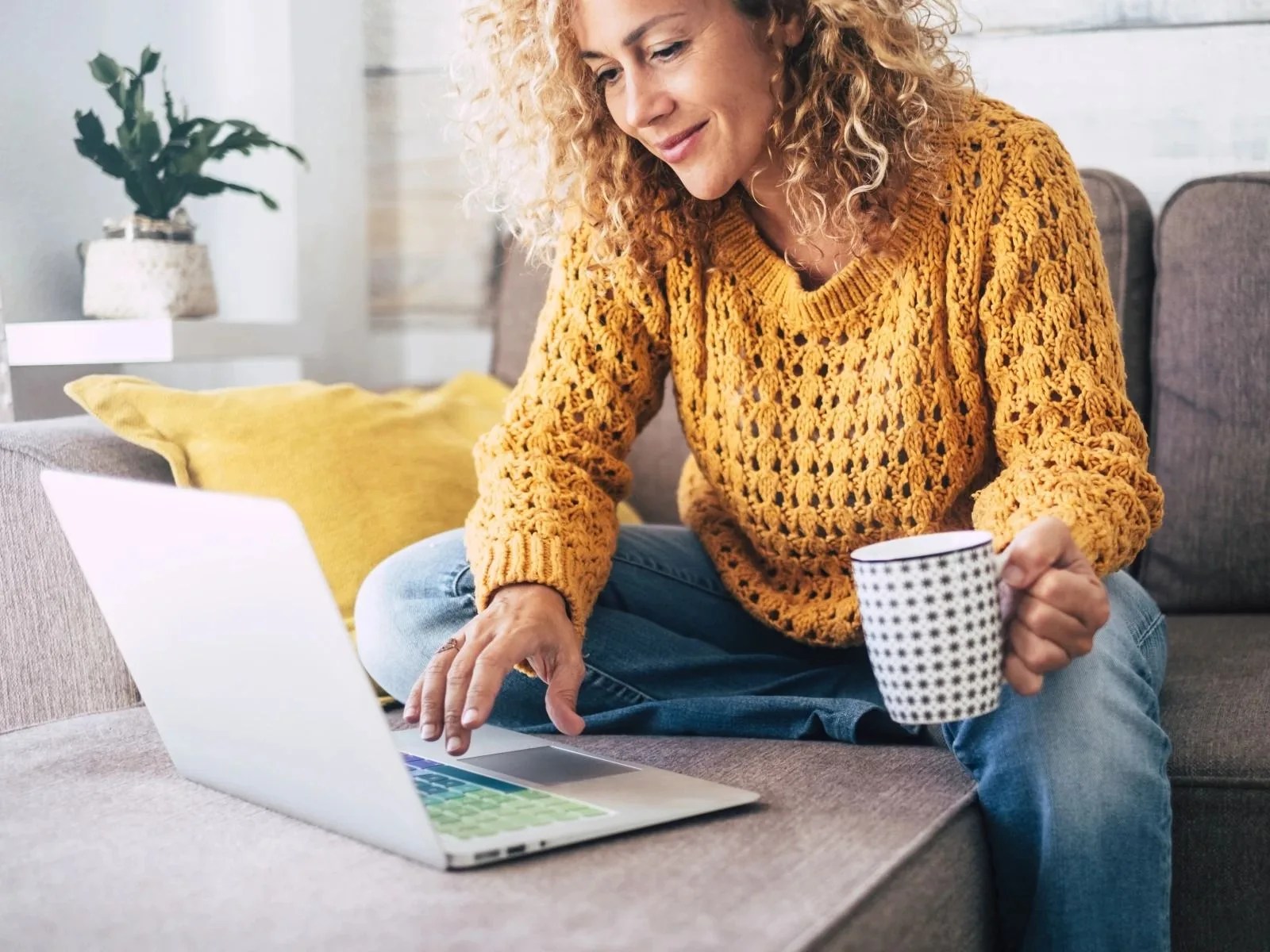 woman looking at a laptop while sitting on a couch drinking coffee