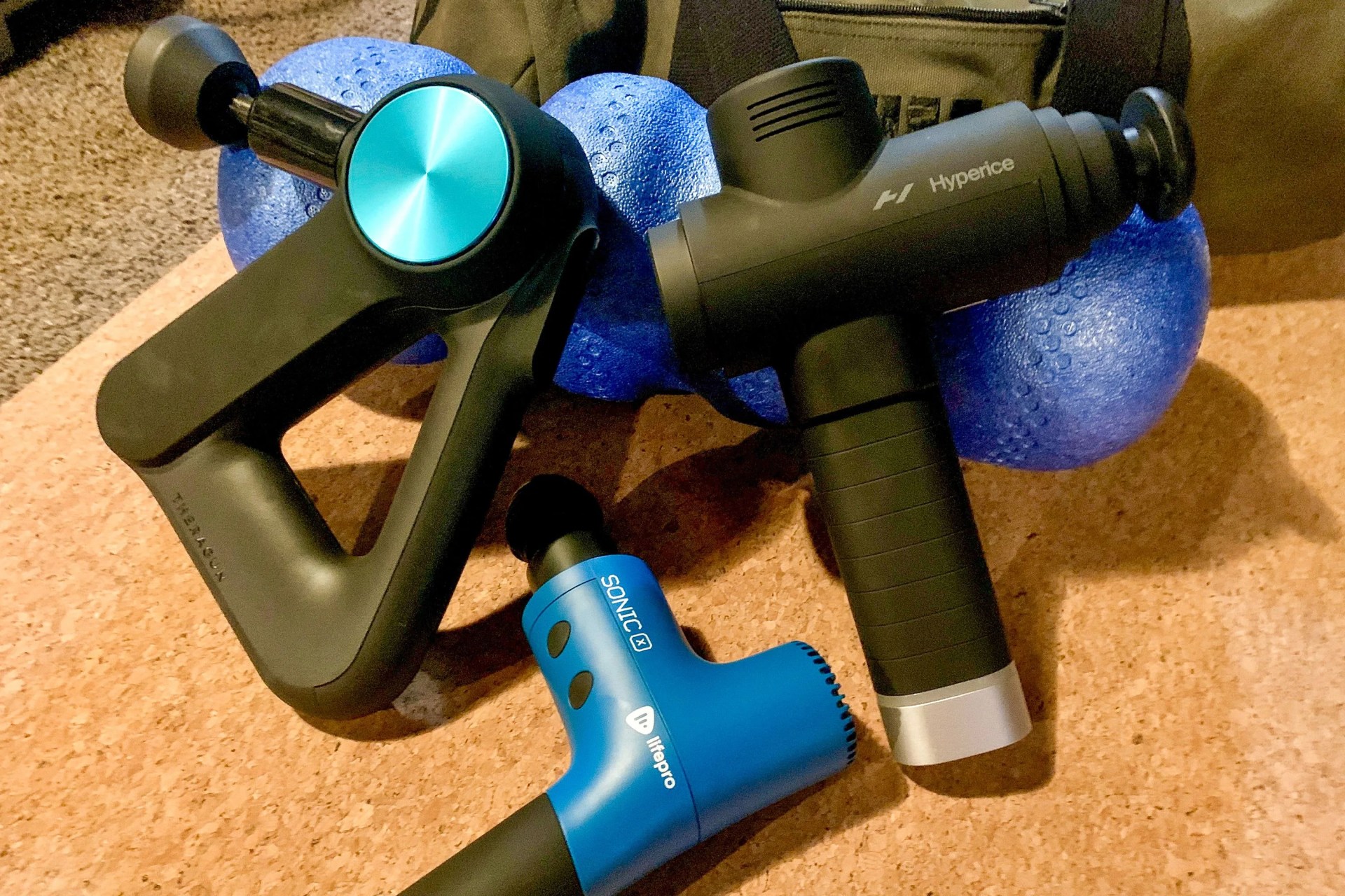 three massage guns on a yoga mat and foam roller