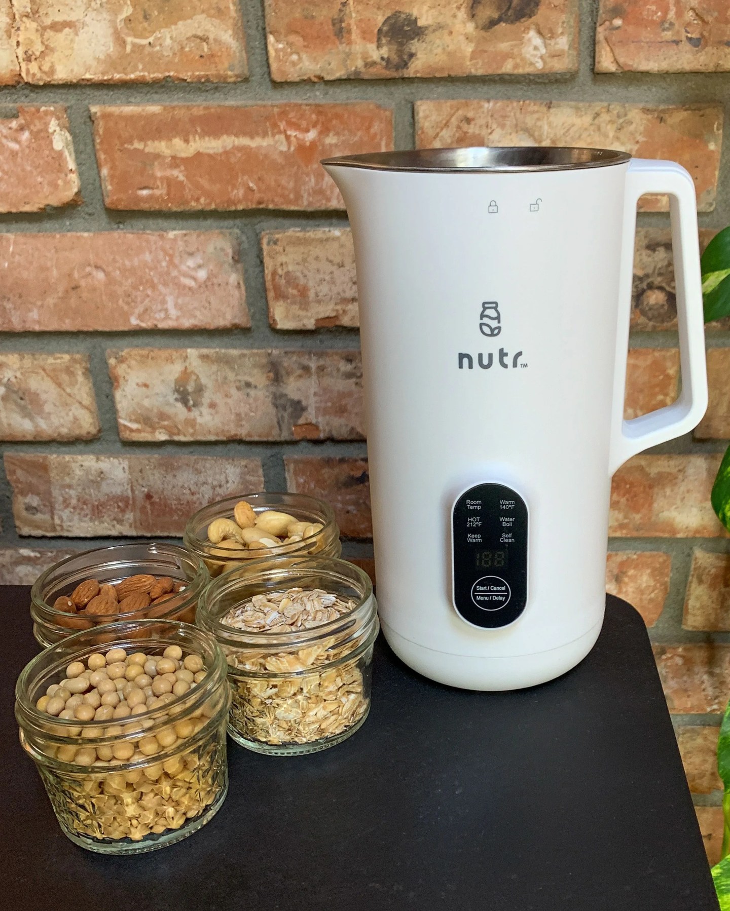 nutr machine on a table with jars of soy beans, nuts, and oats