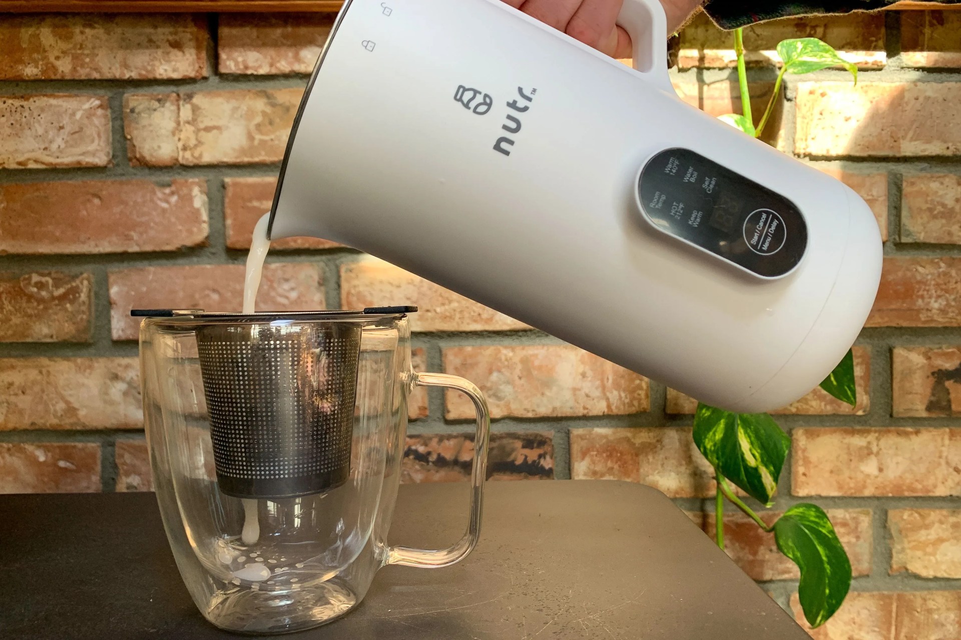 nut milk being poured into a cup with a strainer using the nutr machine