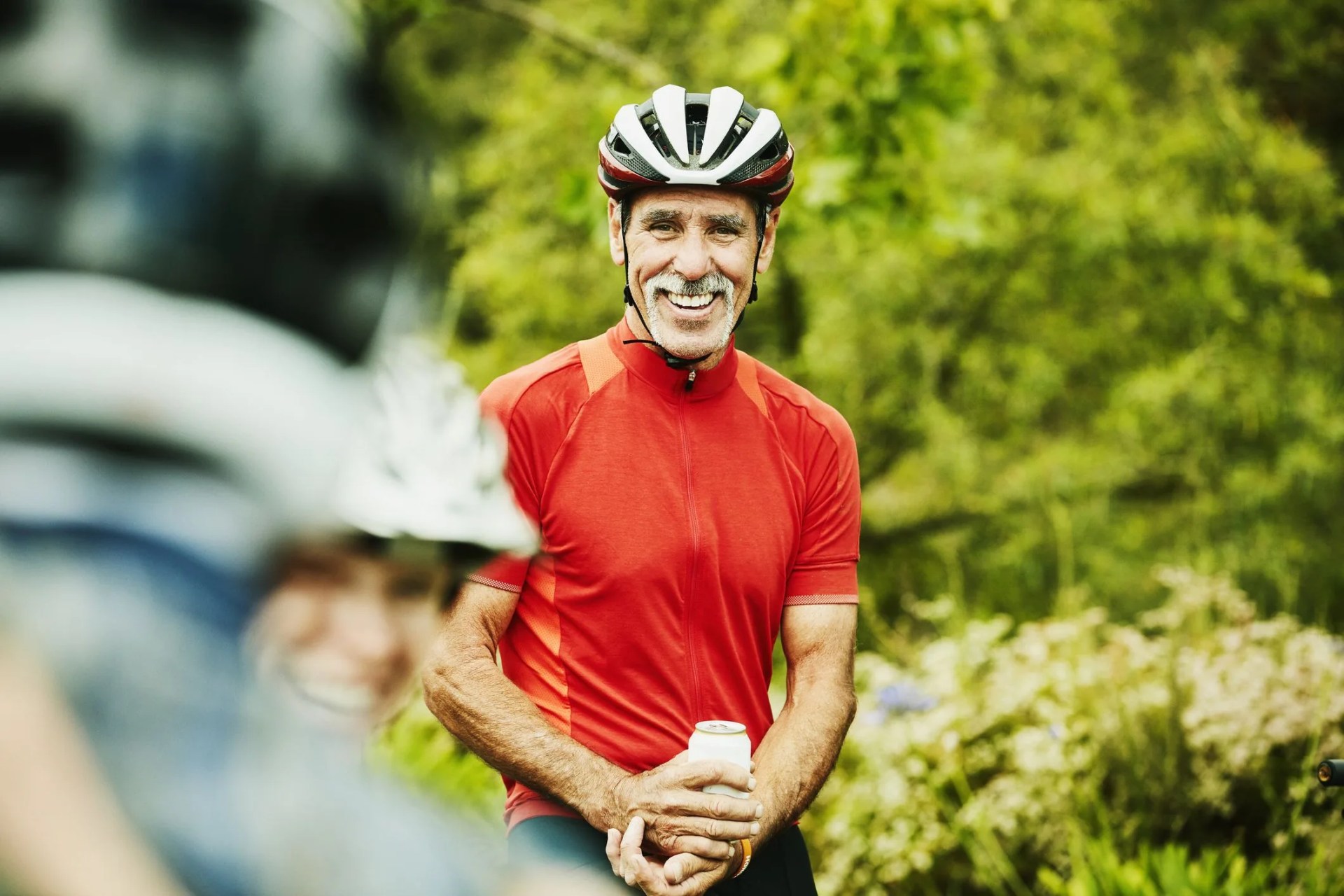 smiling senior man sharing beers with friends after mountain bike ride