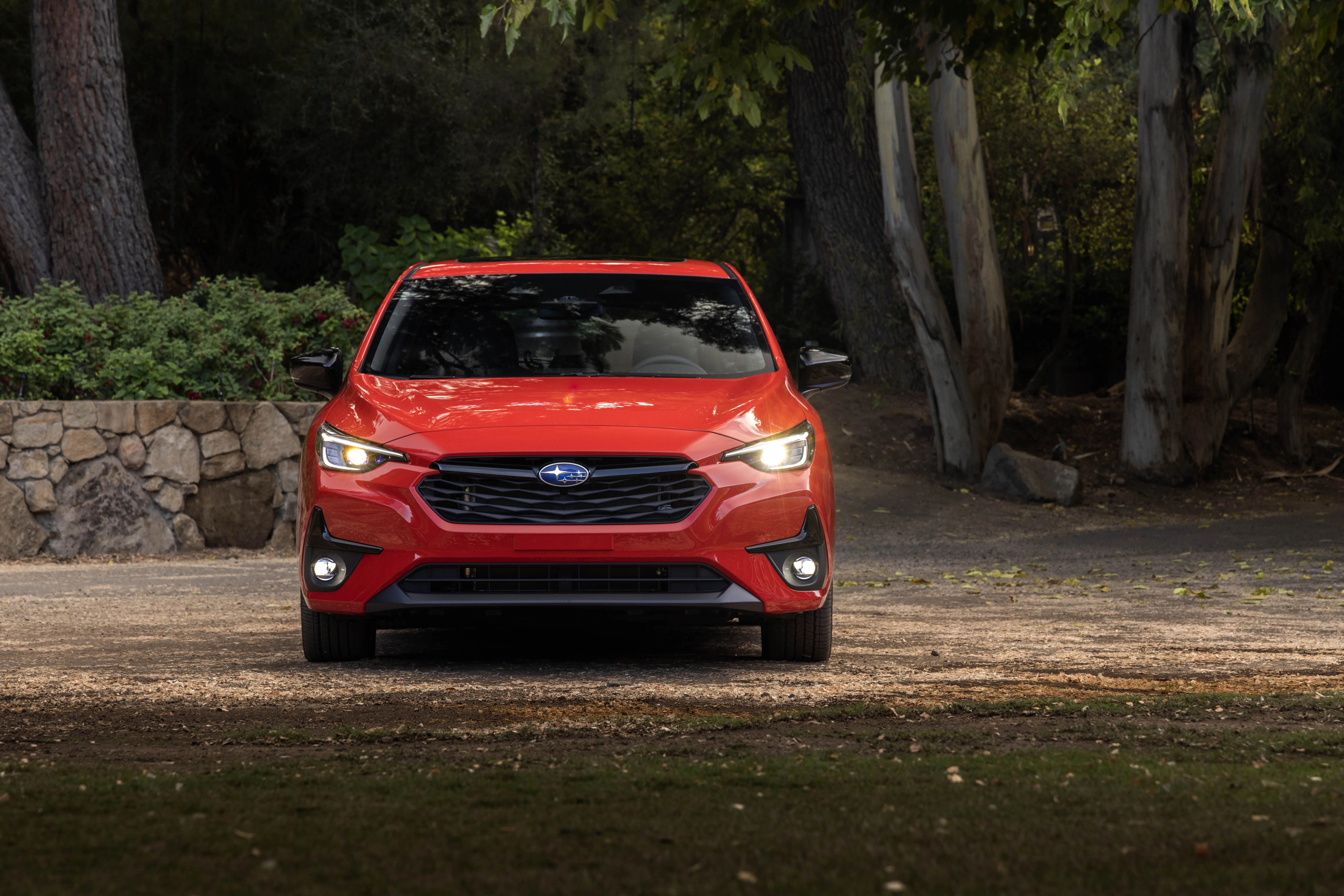 red subaru impreza from the front with a stone wall and trees in the background