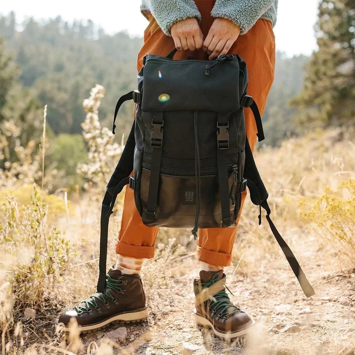 person standing in field holding topo designs’ rover leather pack