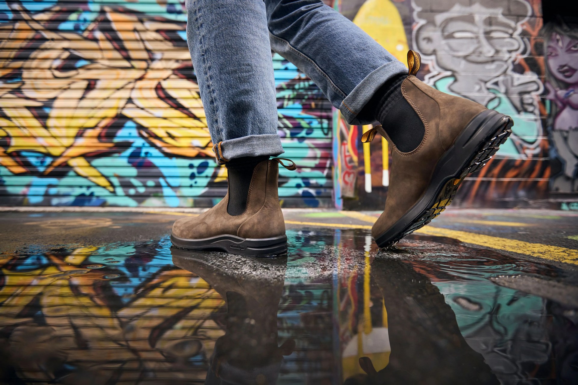 man walking through puddle in an alley filled with graffiti wearing blundstone 2056 men's all terrain chelsea boots in rustic brown