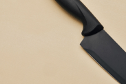 an all black knife on a tan rubber cutting board