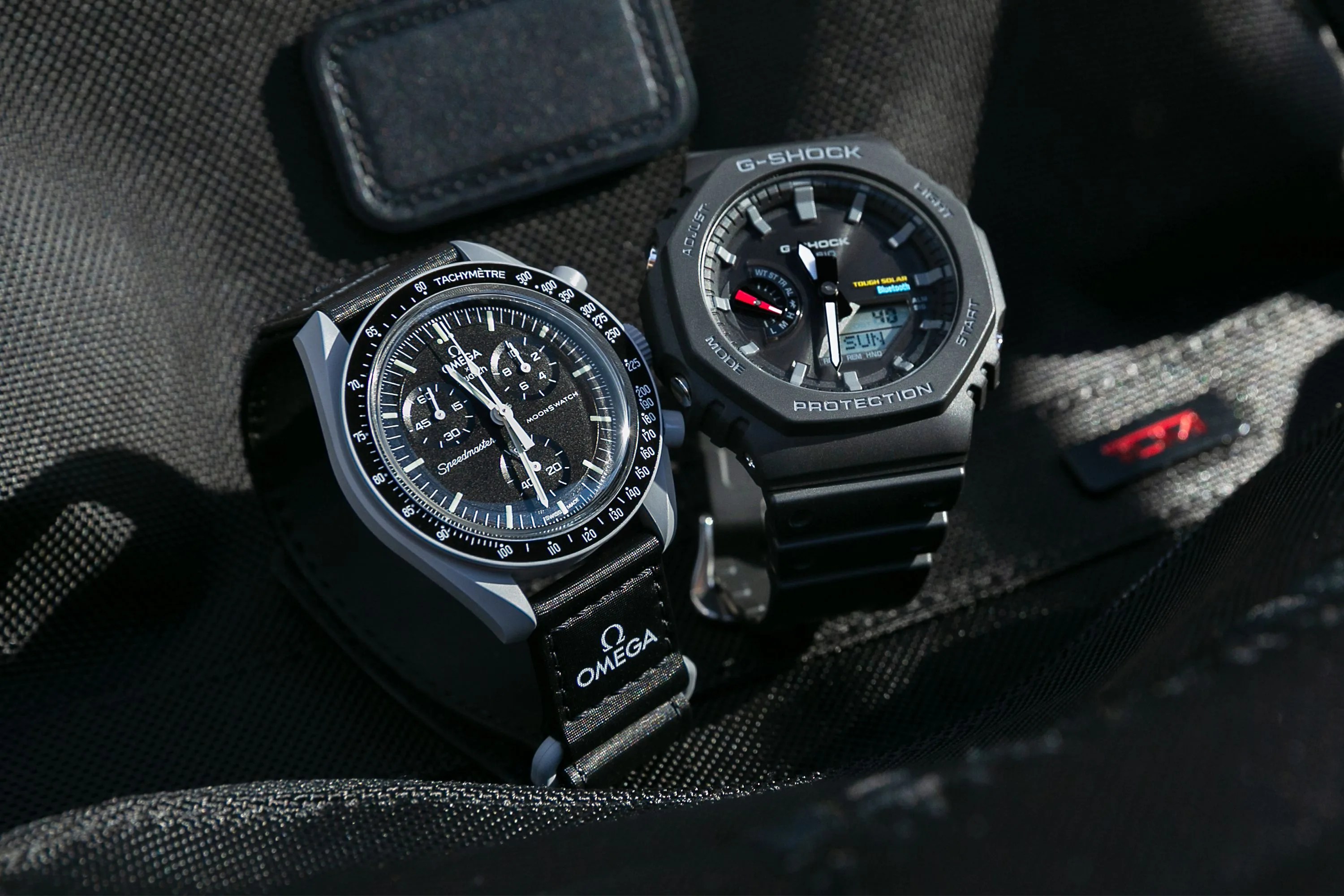 a casio watch next to an omega watch sitting on black fabric