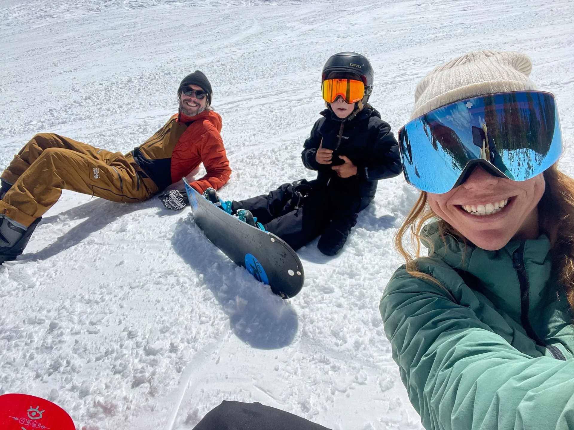 people taking a selfie while sitting on snow with a kid in the middle on a snowboard