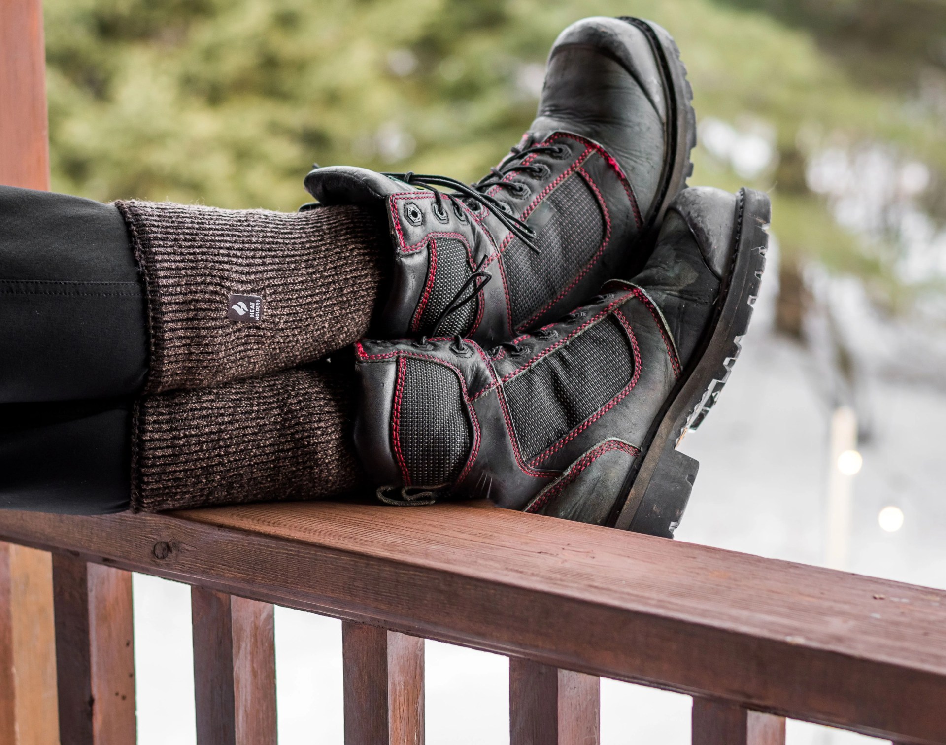 person wearing heat holders muskoka socks under boots propped on fence