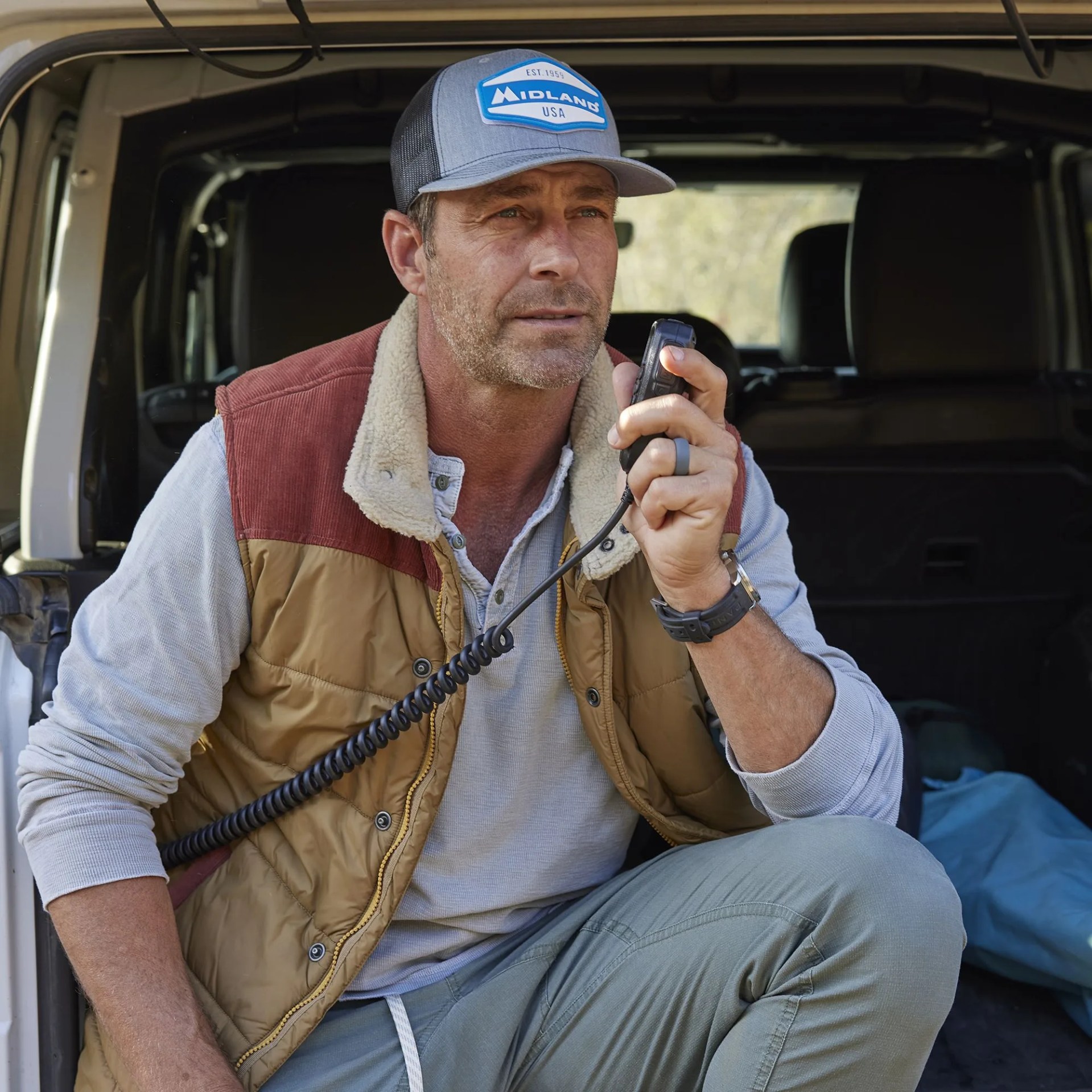 man using midland mxt575 micromobile® two way radio while sitting on back of car