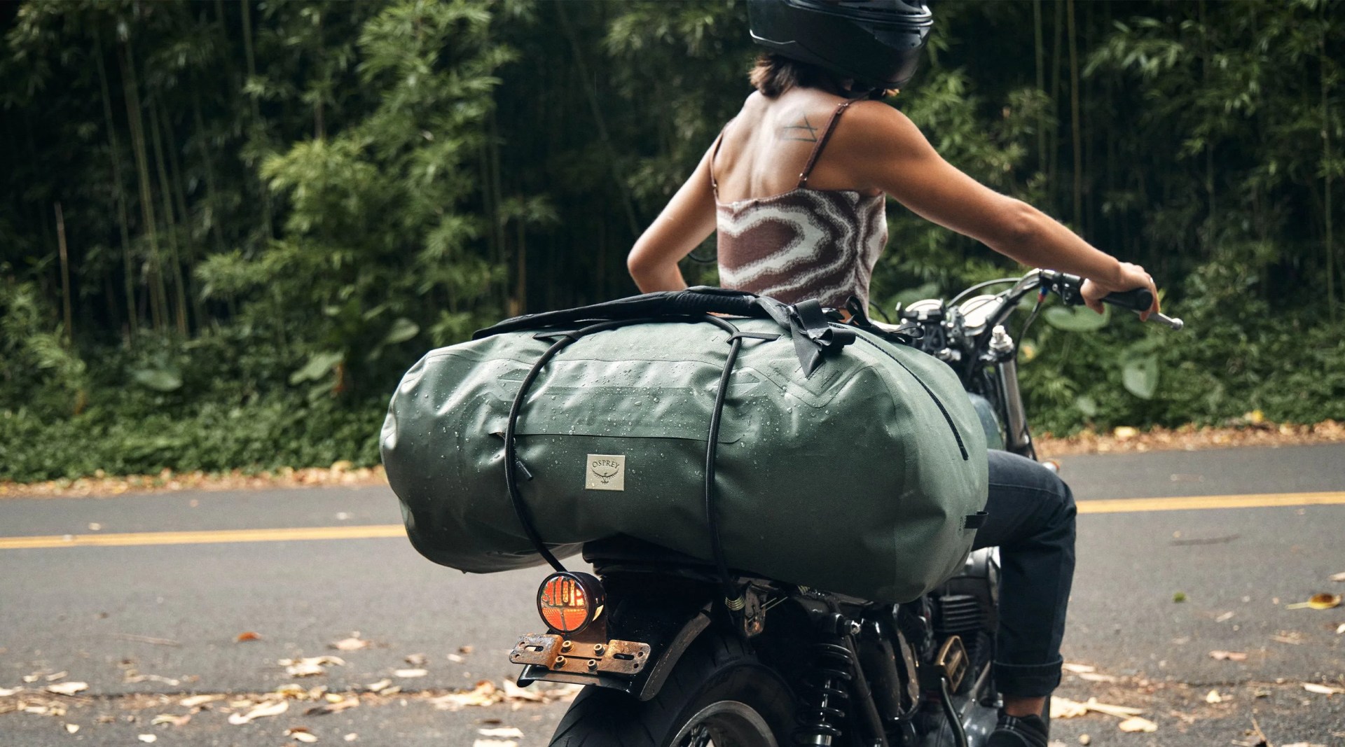woman riding a motorcycle with an osprey duffel bag on the back