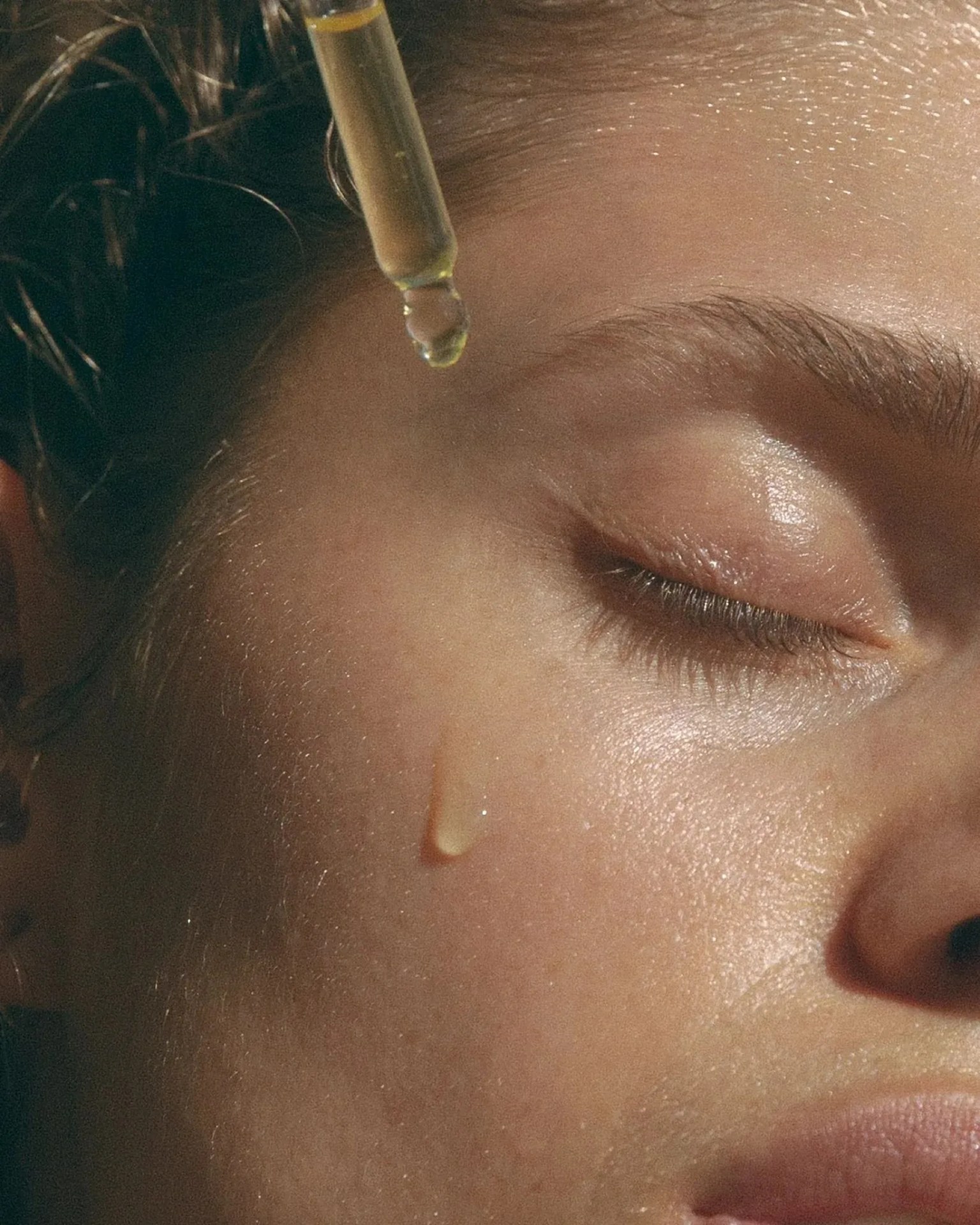 a woman putting a drop of oil on her face
