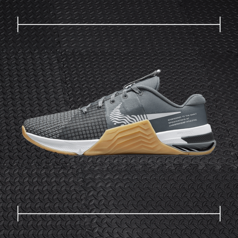 a black nike fitness shoe with gum sole laid overtop a photo of a black rubber gym floor