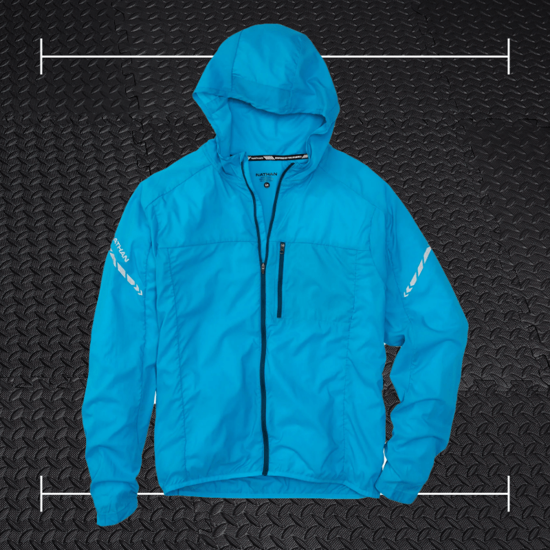 a blue nathan running jacket laid over top a photo of black rubber gym flooring
