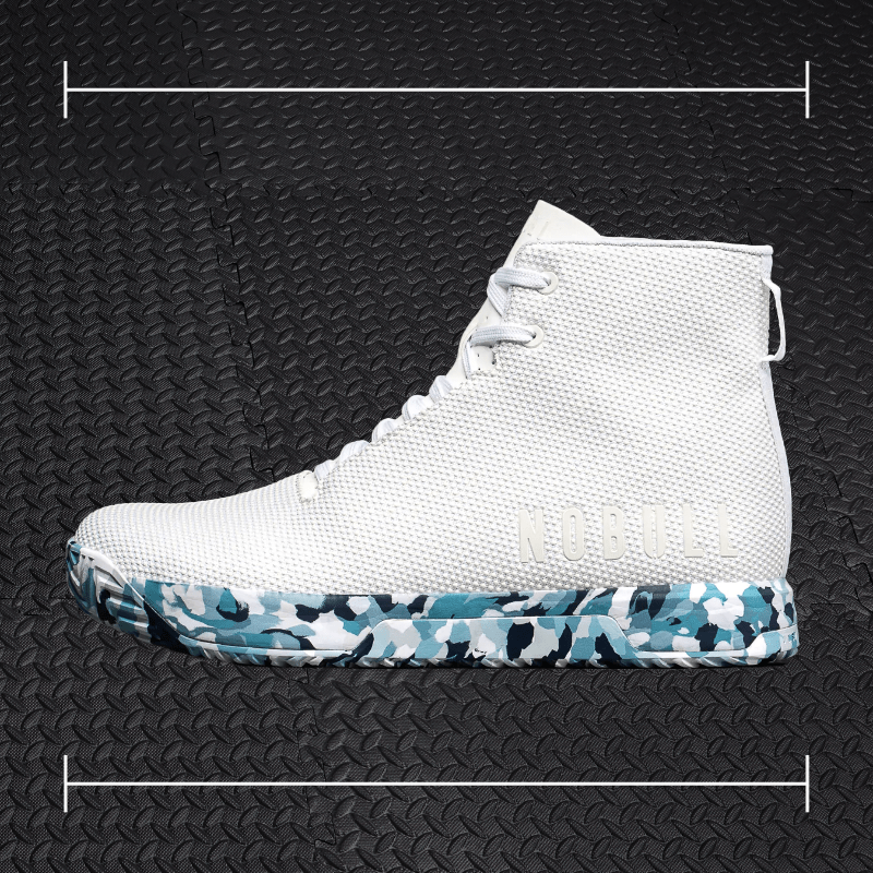 white no bull shoes with blue and black accents laid over top a photo of black rubber gym flooring