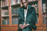 a man wearing a green corduroy suit sitting in front of a book case