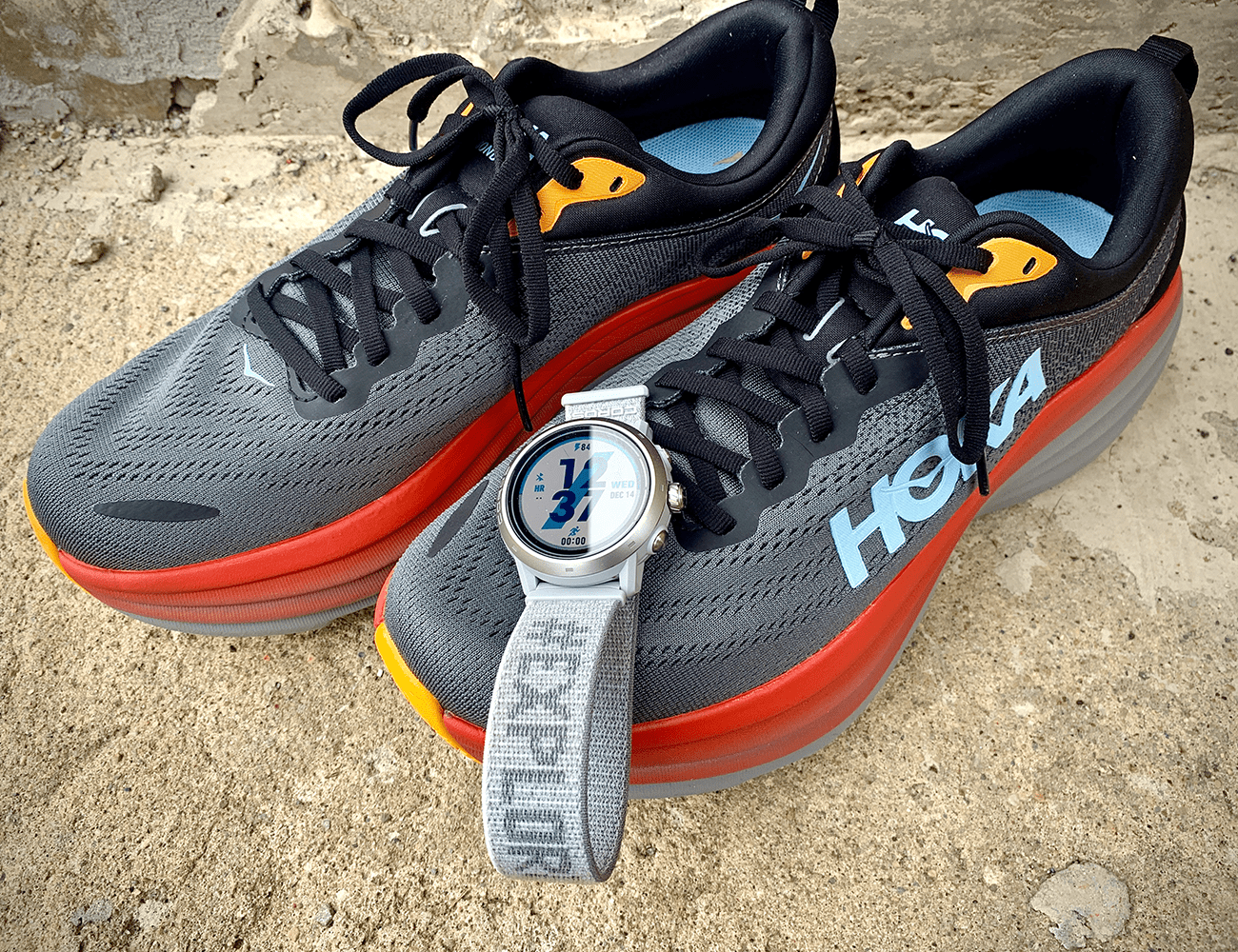 a silver coros apex 2 laid over a grey orange hoka running shoe