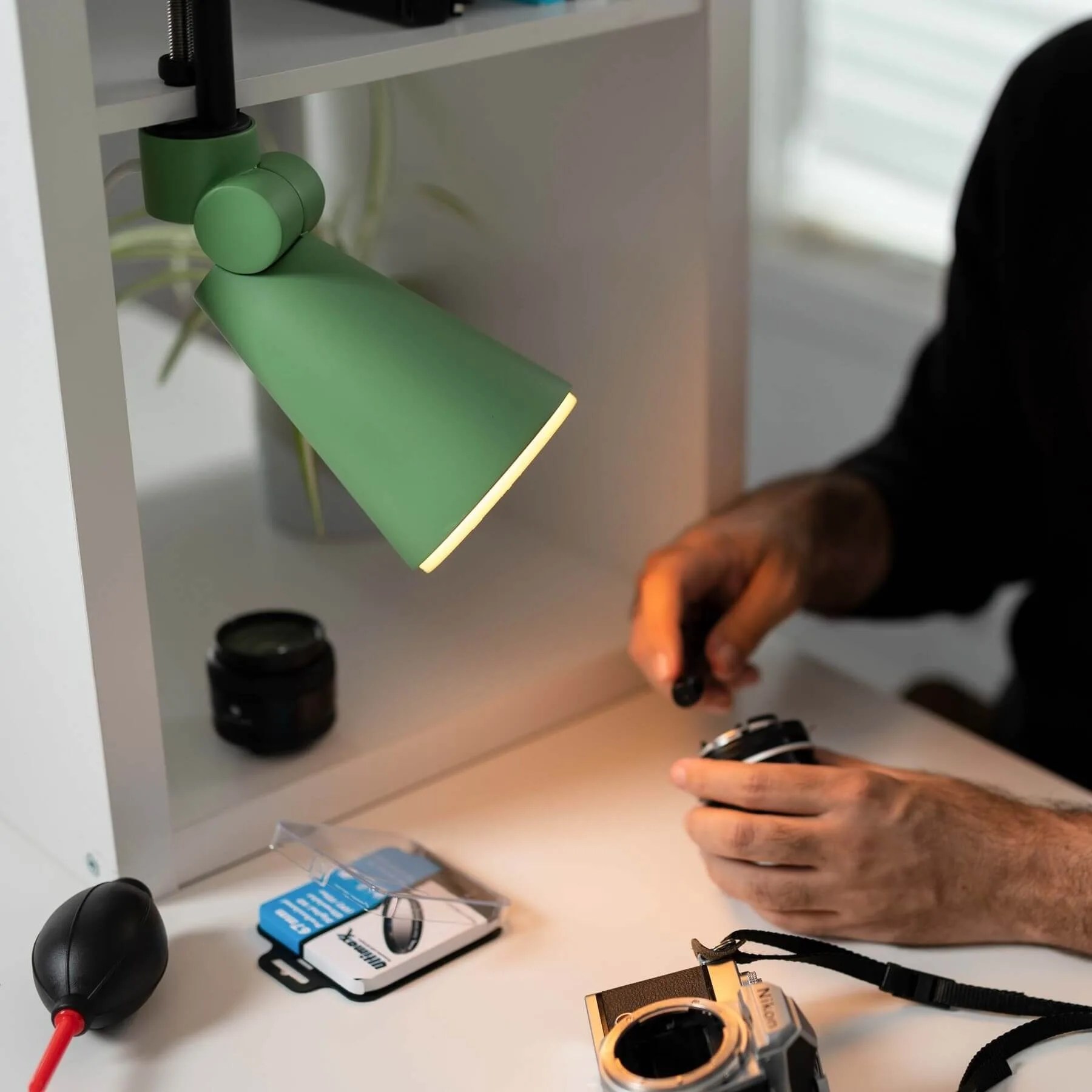 a clamp light illuminates a person cleaning a camera lens
