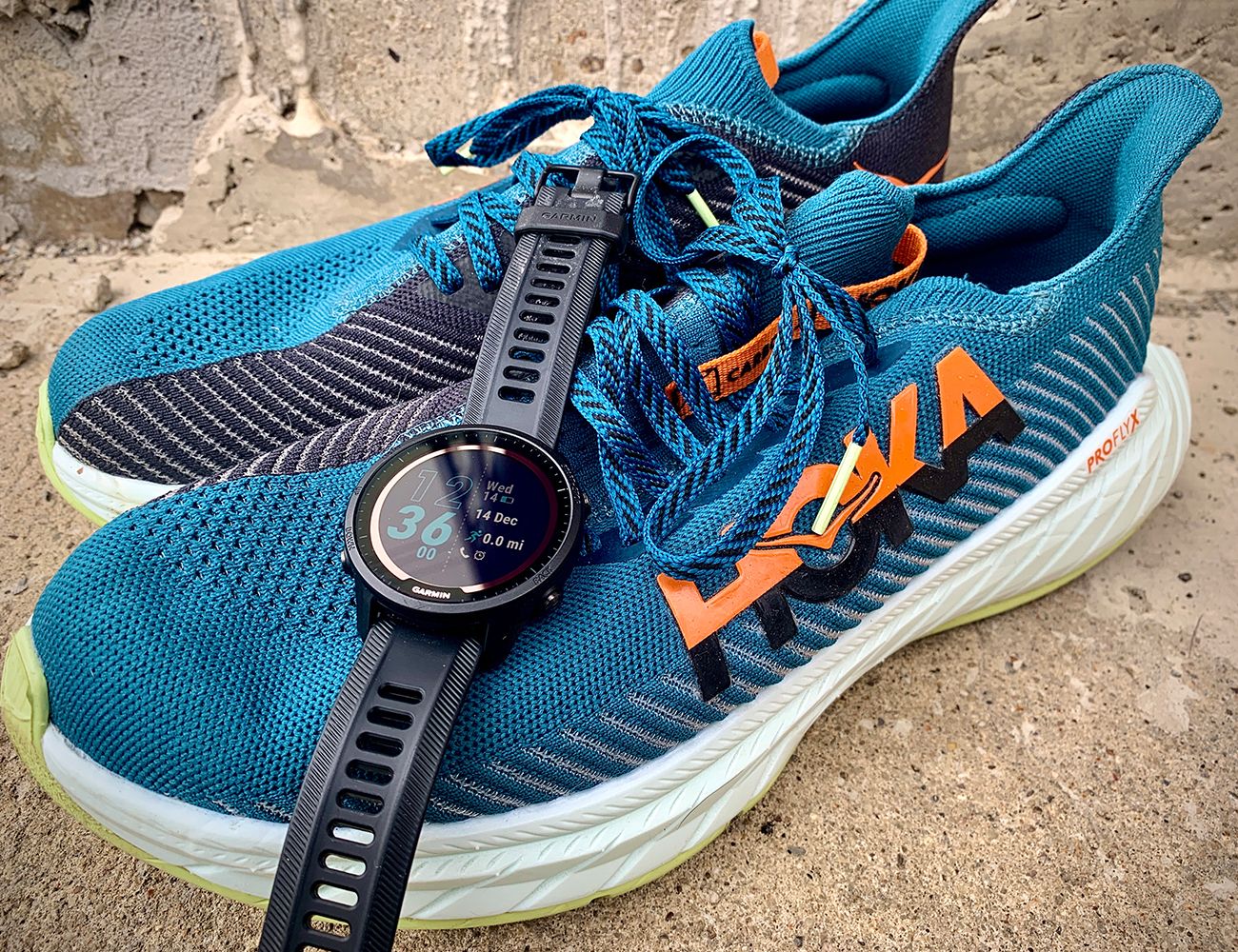 a black garmin forerunner 955 solar watch laid over a blue hoka running shoe