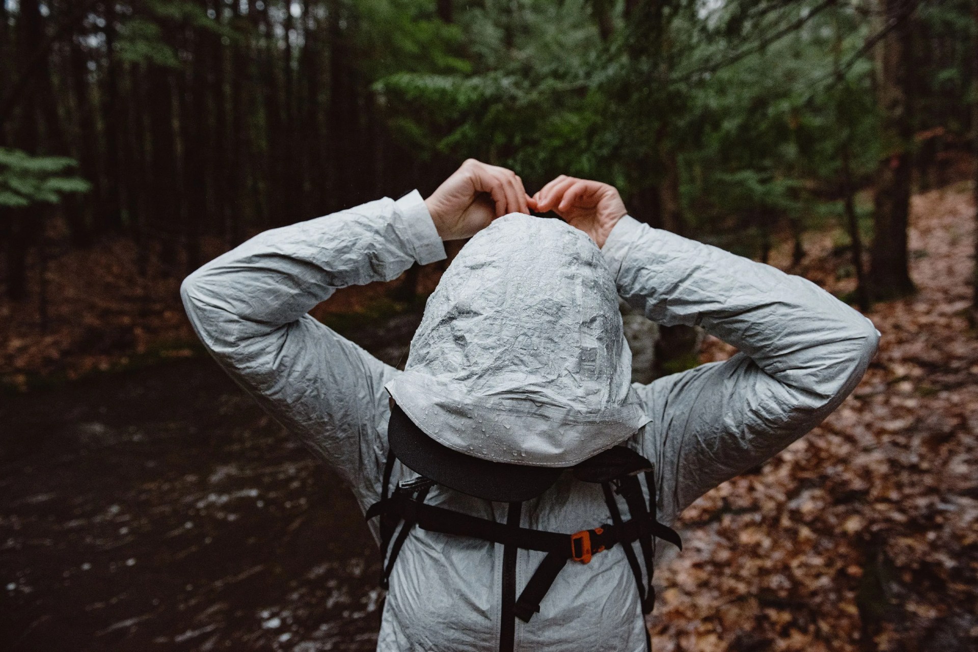 a person tightening a hood on a rain coat while standing in the woods
