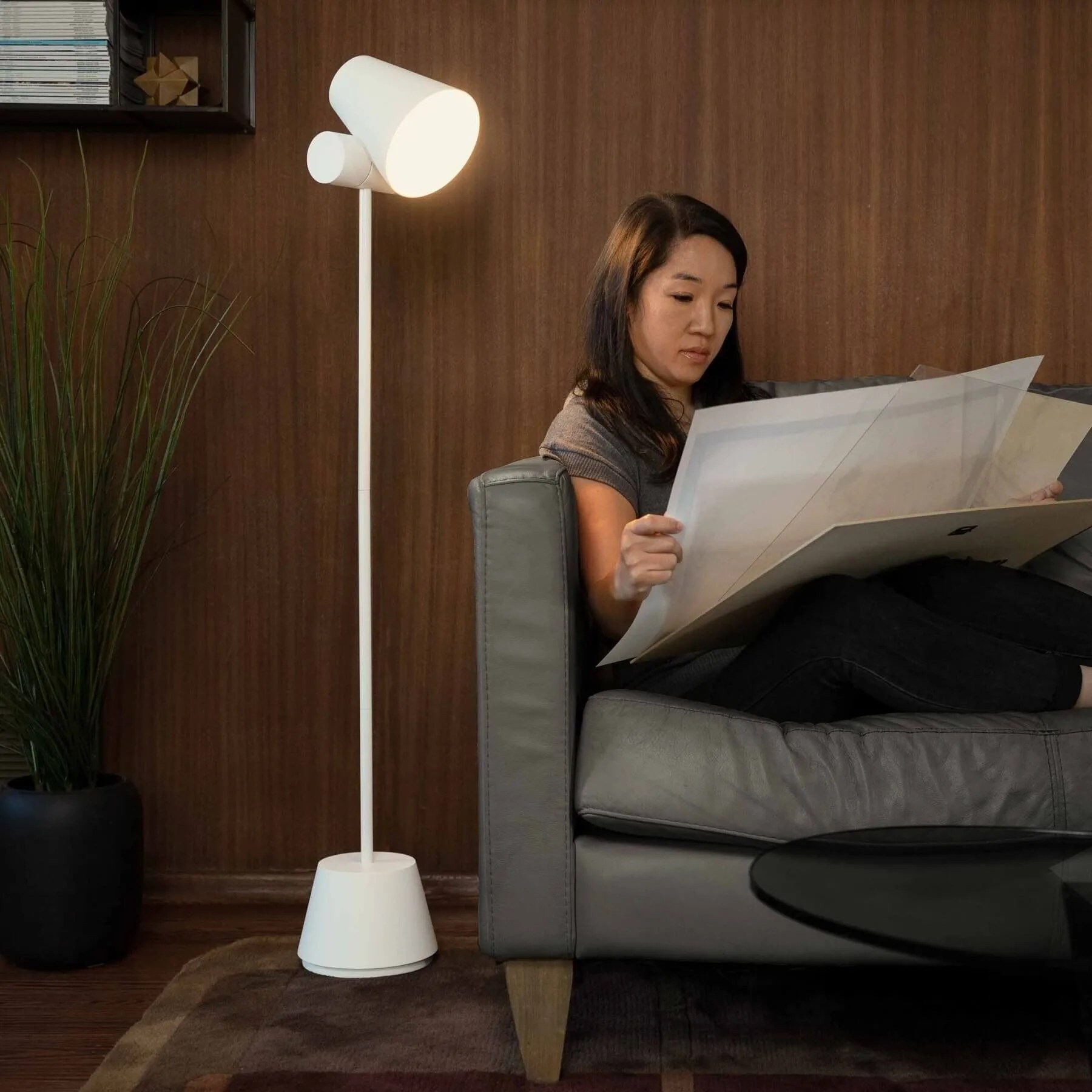 a woman sitting on a couch reading with a lamp