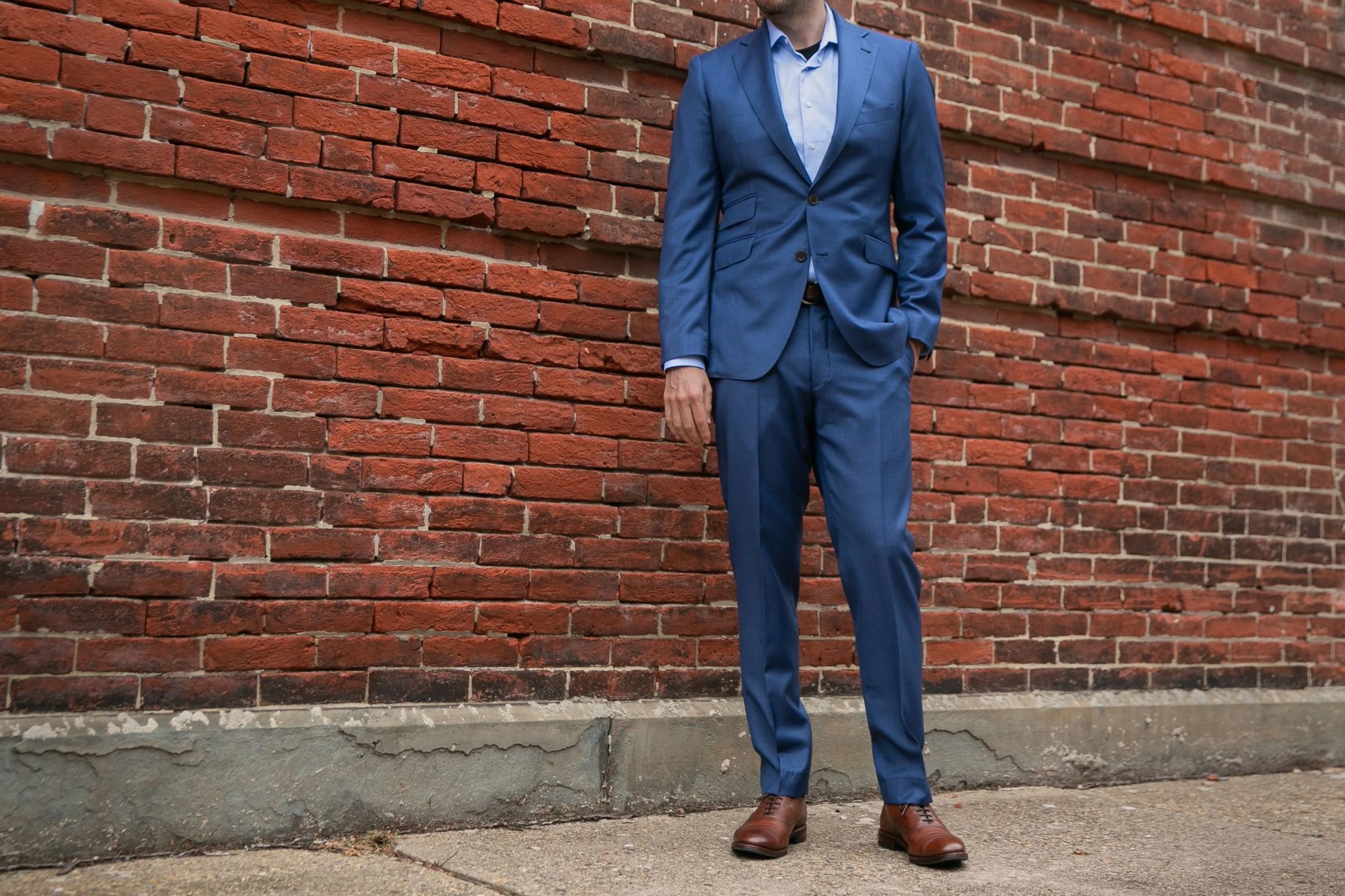a man wearing a custom blue suit in front of a brick wall