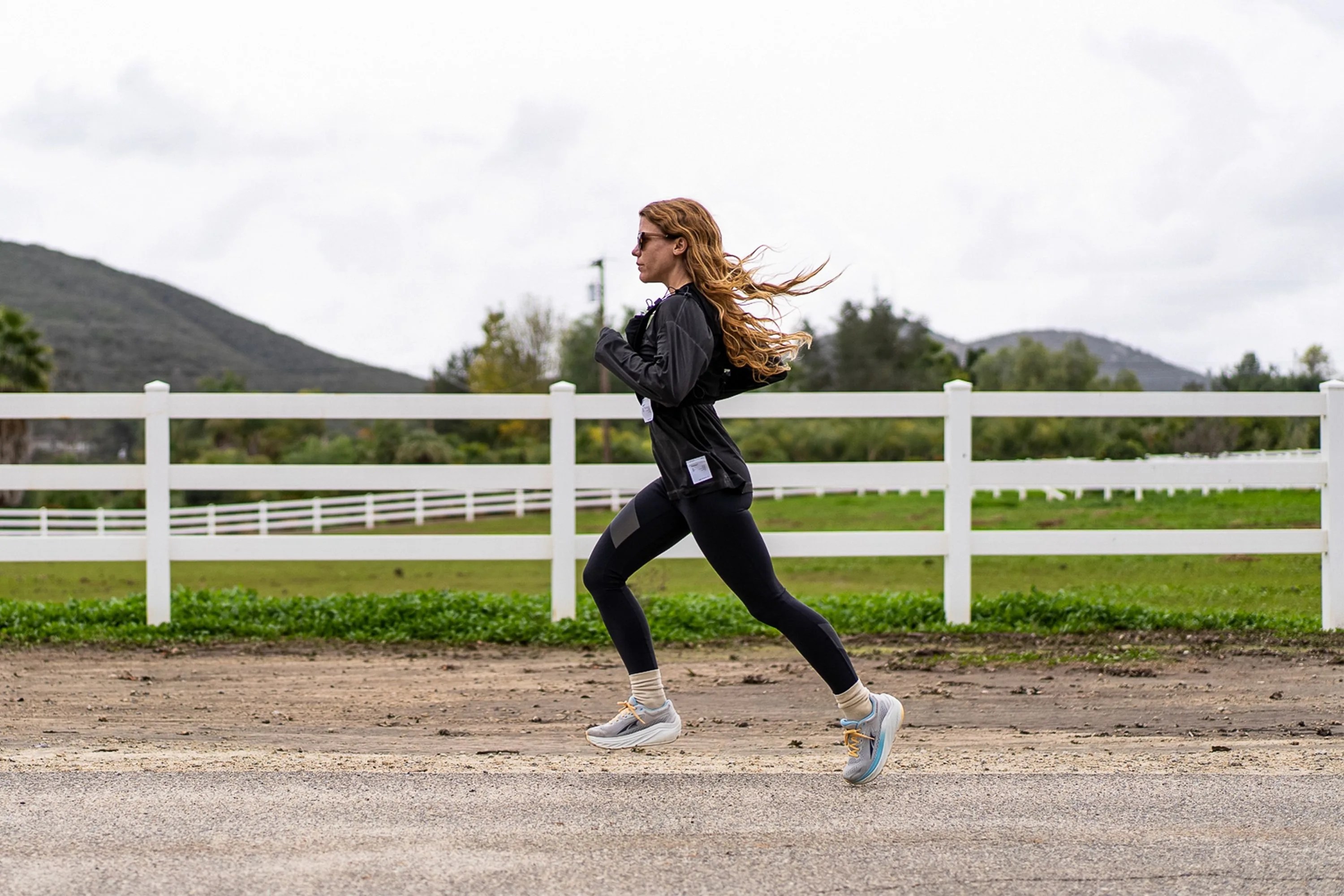 a woman running by a horse pasture
