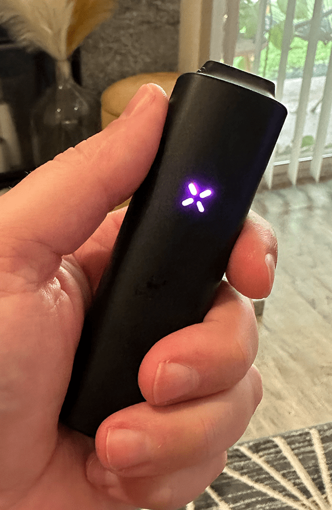 a hand holding a black pax plus showing a purple light on the front
