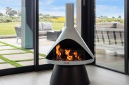 an indoor ventless fireplace in a corner of a house with floor to ceiling glass windows