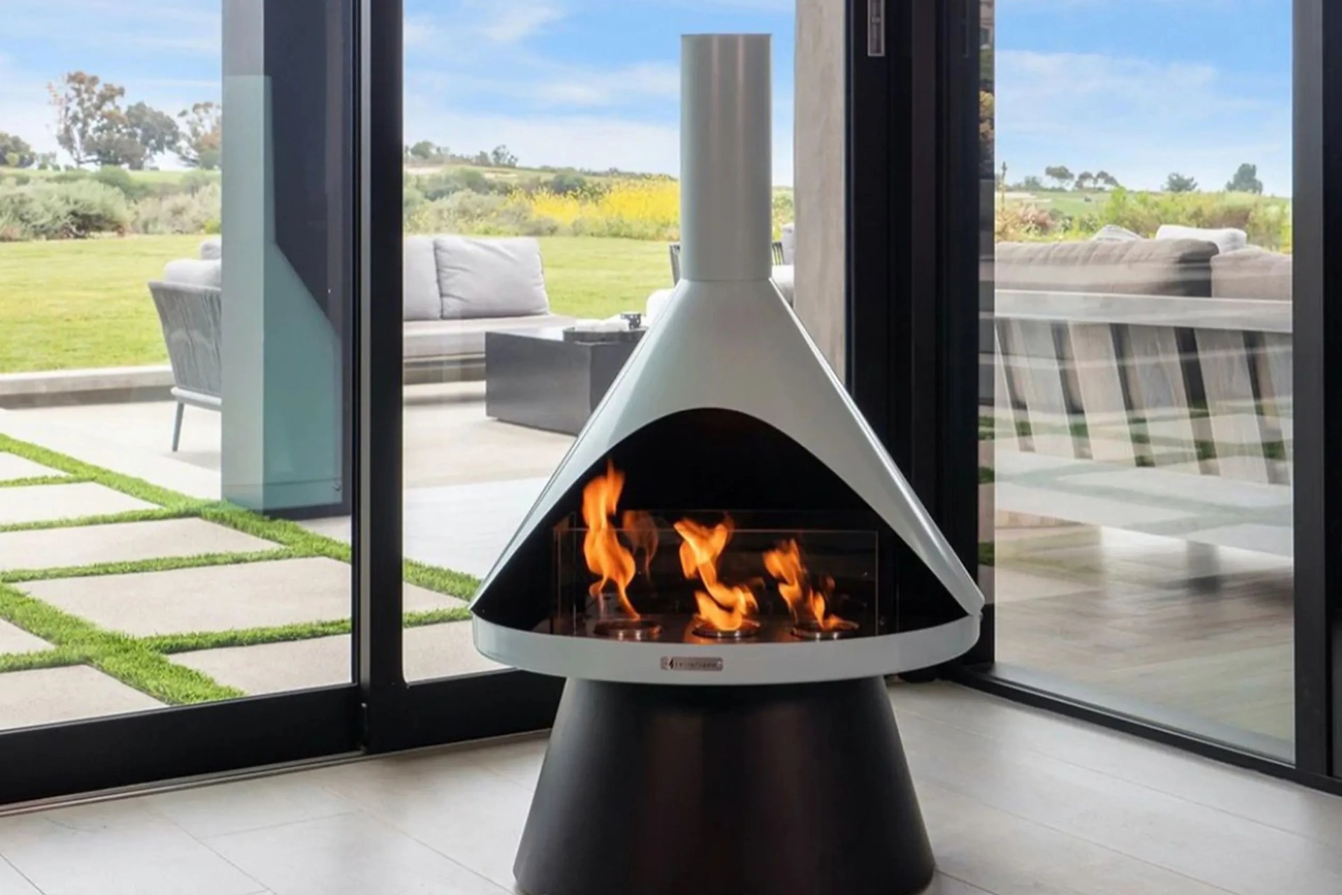 an indoor ventless fireplace in a corner of a house with floor to ceiling glass windows