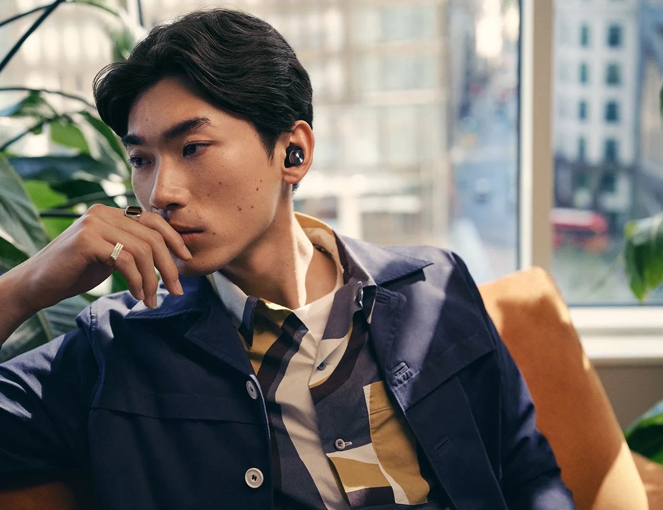 a man sitting on a couch looking to his right with a wireless earbud in his left ear